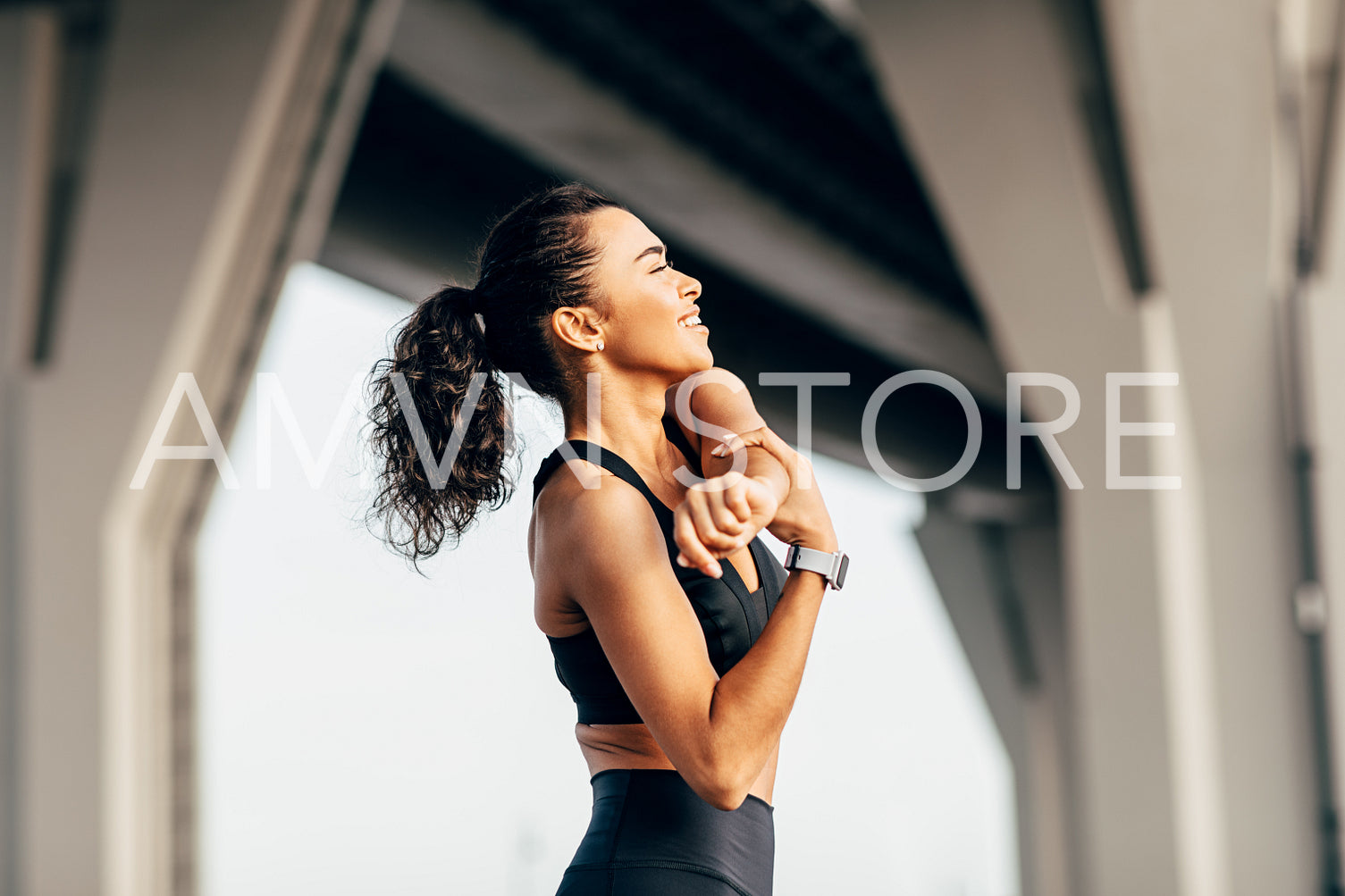 Side view of a fitness woman doing arms stretching exercise under highway outdoors	