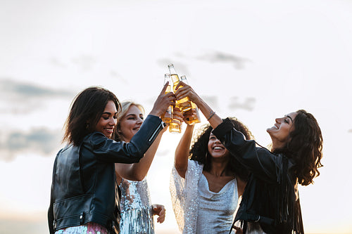 Four happy friends toasting with beer bottles at sunset