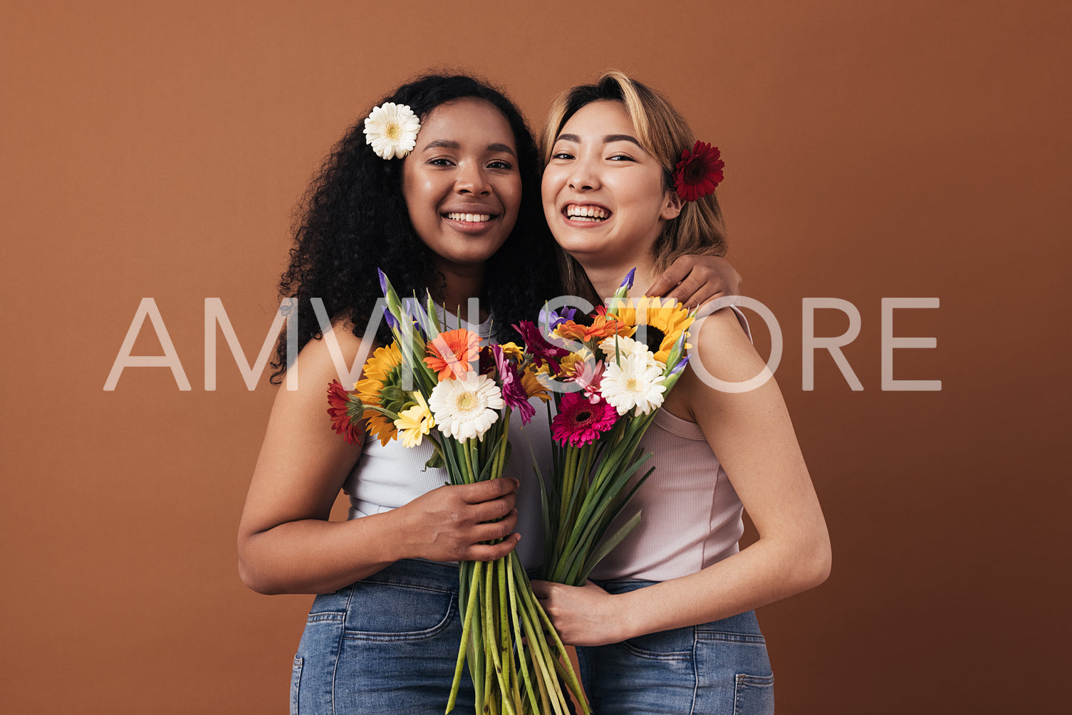 Two young women of different races with bouquets and flowers in their hair posing against a brown background