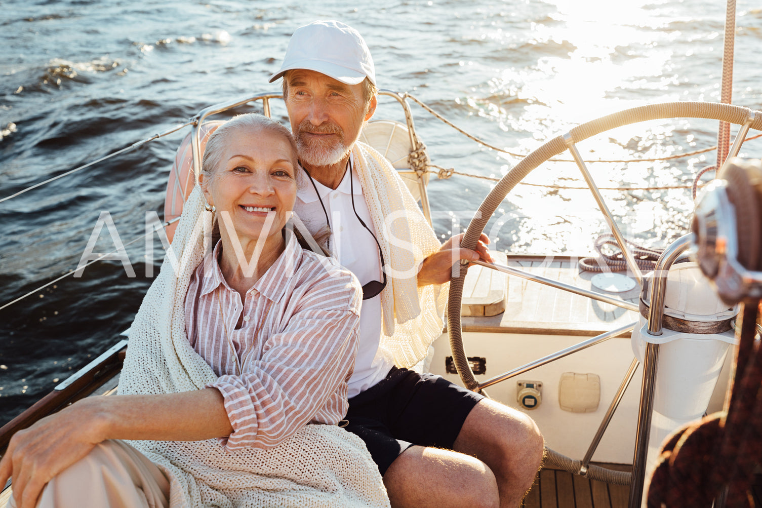 Smiling mature woman looking at camera while her husband steering a sailboat. Two senior people enjoying a vacation on yacht.	