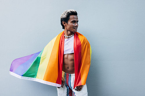 Handsome muscular man posing against grey wall with rainbow flag