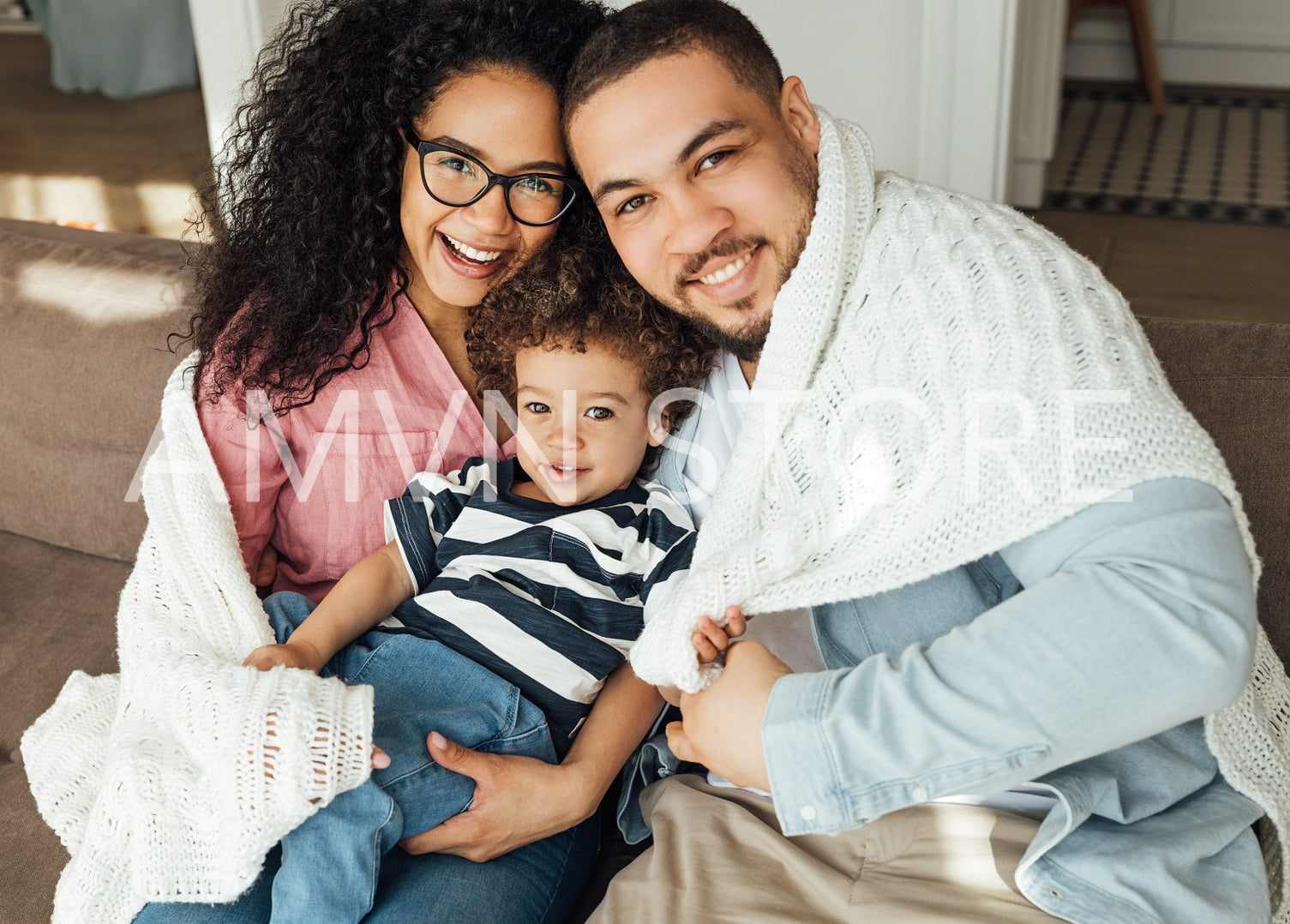 Mother, father, and their cute son looking at camera. Family of three sitting at home wrapped in white plaid.	