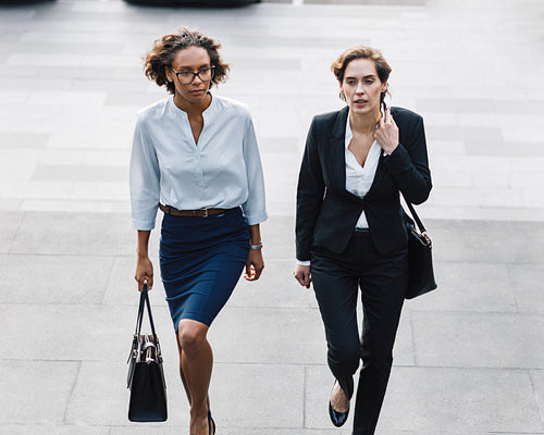 Two women in office wear stepping up on stairs in the city