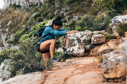 Side view of woman hiker grabs a big rock to helps her climbing up