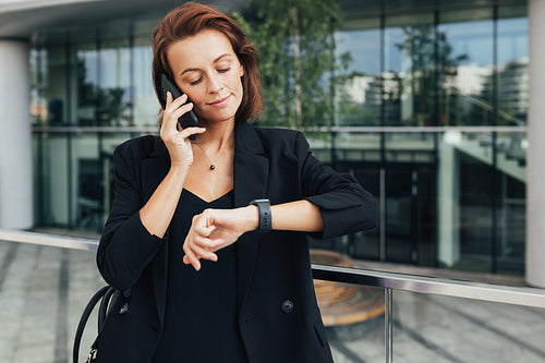 Middle-aged businesswoman looking at her smartwatch while talking on mobile phone