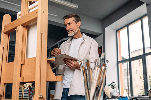 Male painter standing in his studio at an easel and looking on canvas