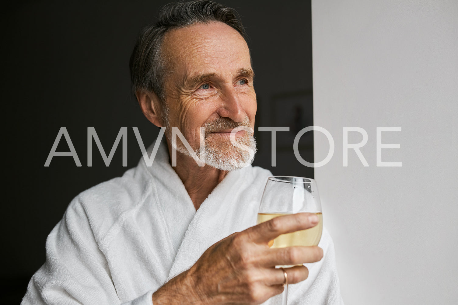 Close up of smiling mature man wearing white bathrobe holding wineglass looking away	