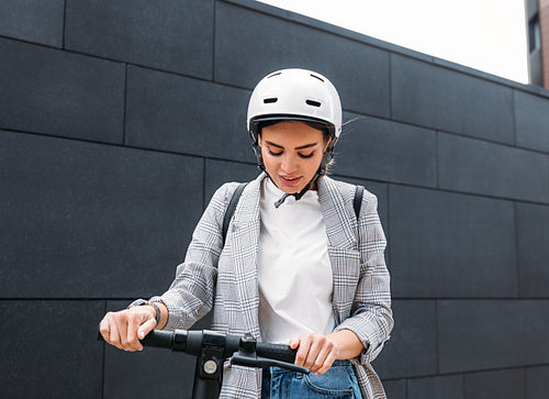 Young caucasian woman wearing white cycling helmet holding handlebar of electric scooter