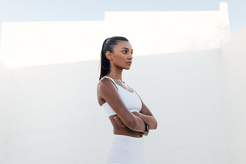 Side view of a confident female athlete standing outdoors. Fitness woman with crossed hands standing confidently during exercises.