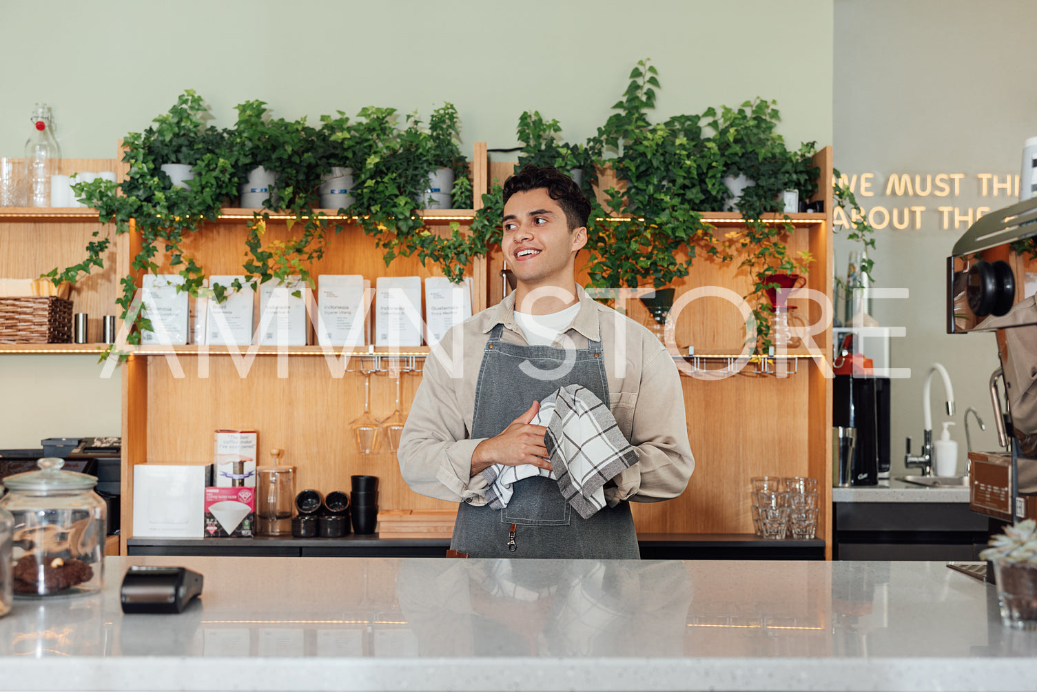 Smiling male bartender wiping a glass and looking away. Barista in a coffee shop holding a towel.