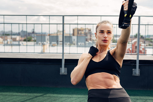 Fitness woman in sportswear exercising on rooftop. Young athlete using suspension rope for push ups.