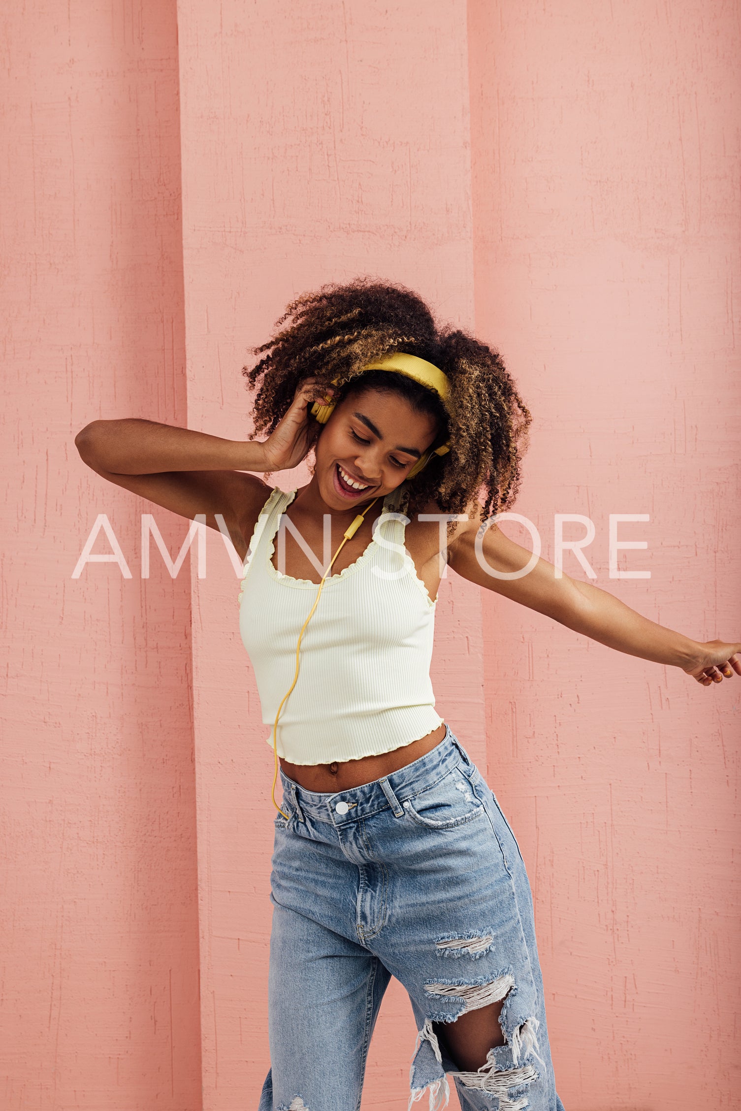 Young woman wearing yellow headphones at pink wall and dancing