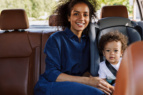 Young mother sitting with her son on backseat. Little boy in kid car seat looking at the camera.