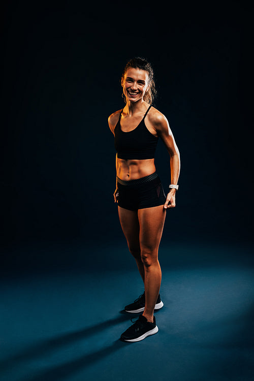 Young fit runner in sportswear standing on dark background in studio and looking at camera