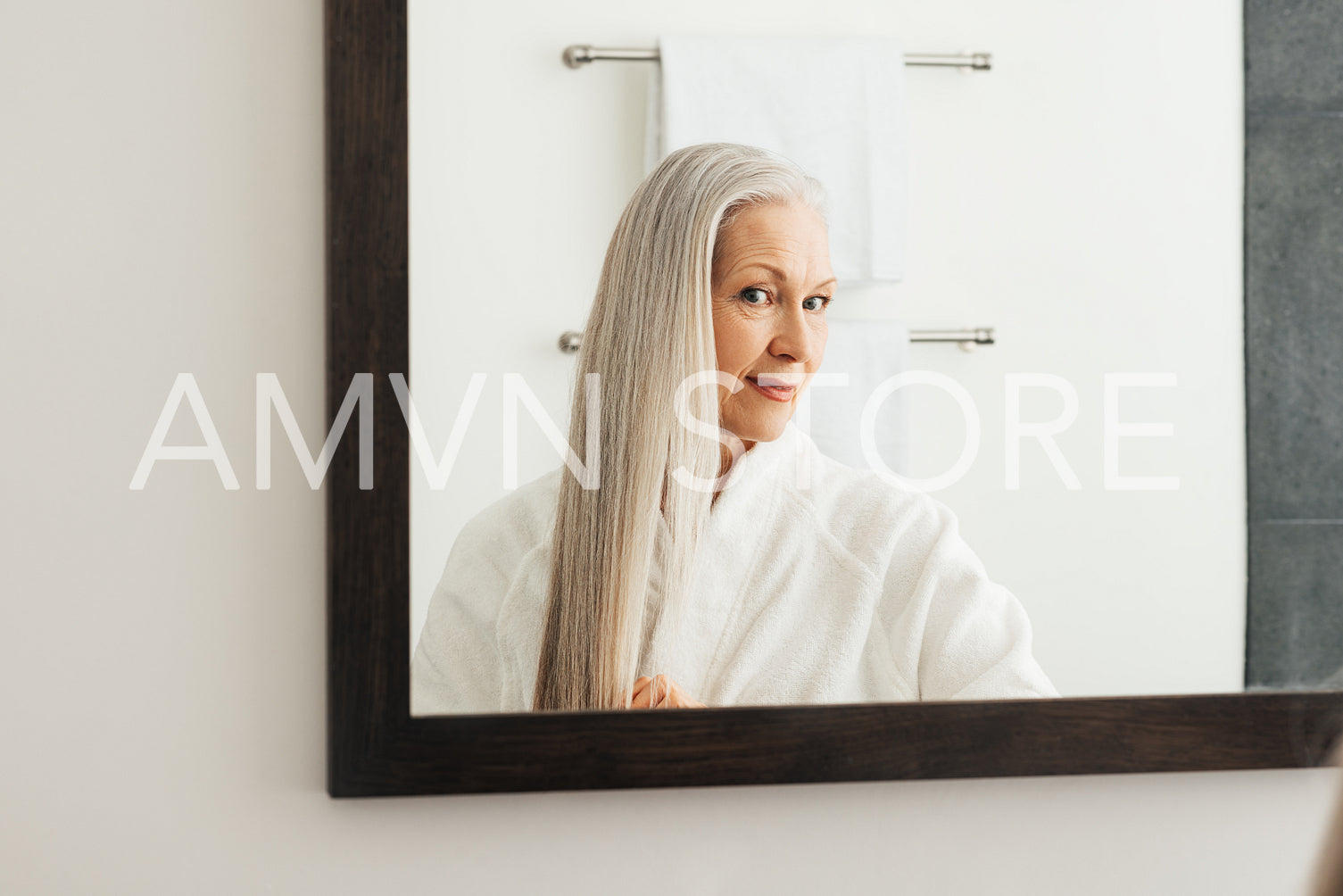 Portrait of an aged woman with long grey hair. Female looking in the mirror admires her hair.