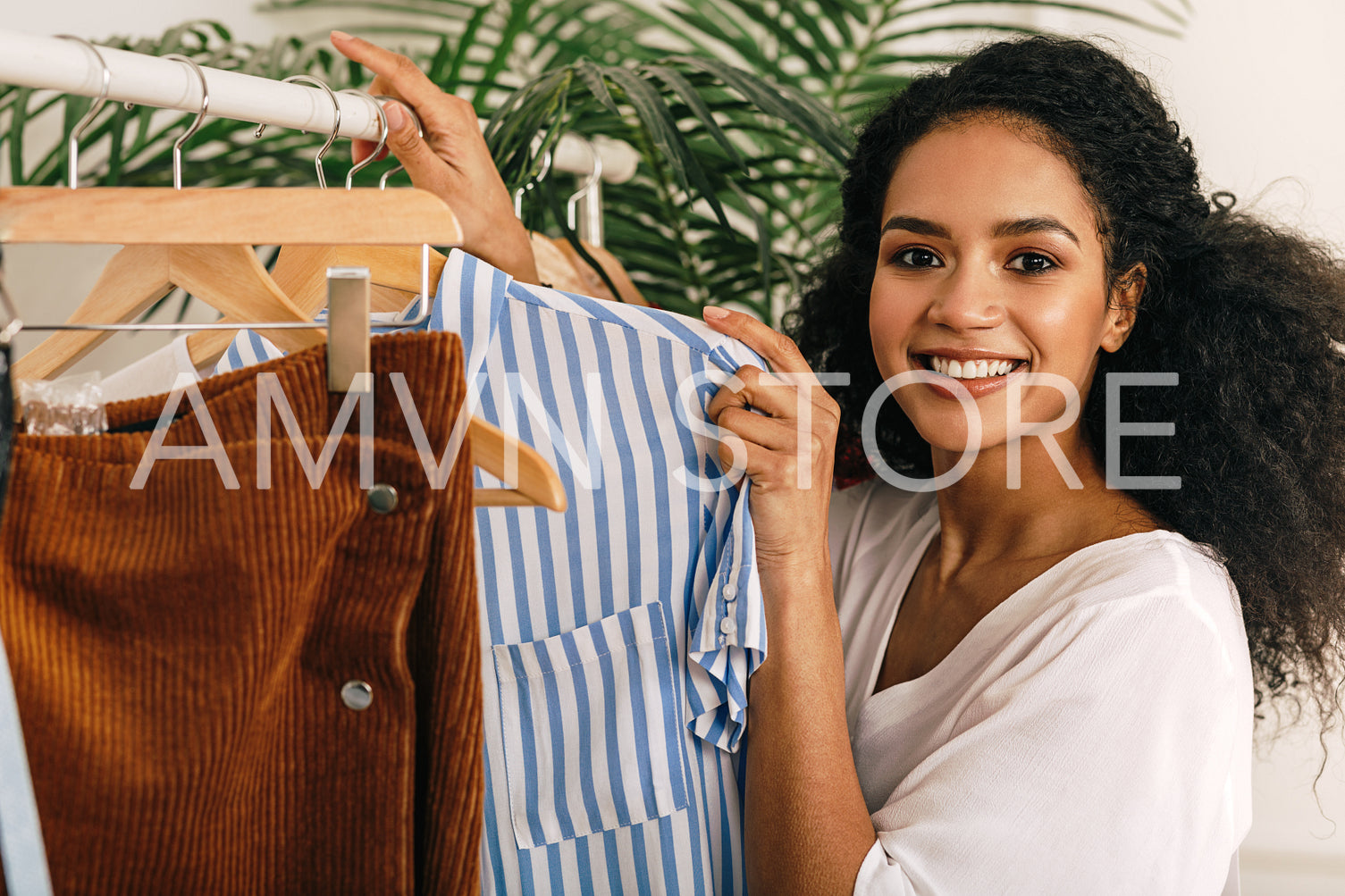 Happy beautiful woman standing at clothes rack and holding shirt	