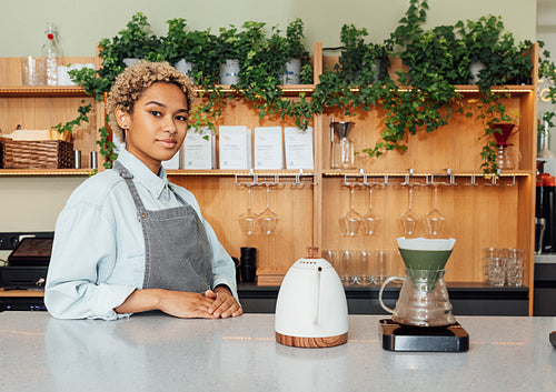 Young woman in apron working as a barista standing at the counter with a kettle, filter and scales