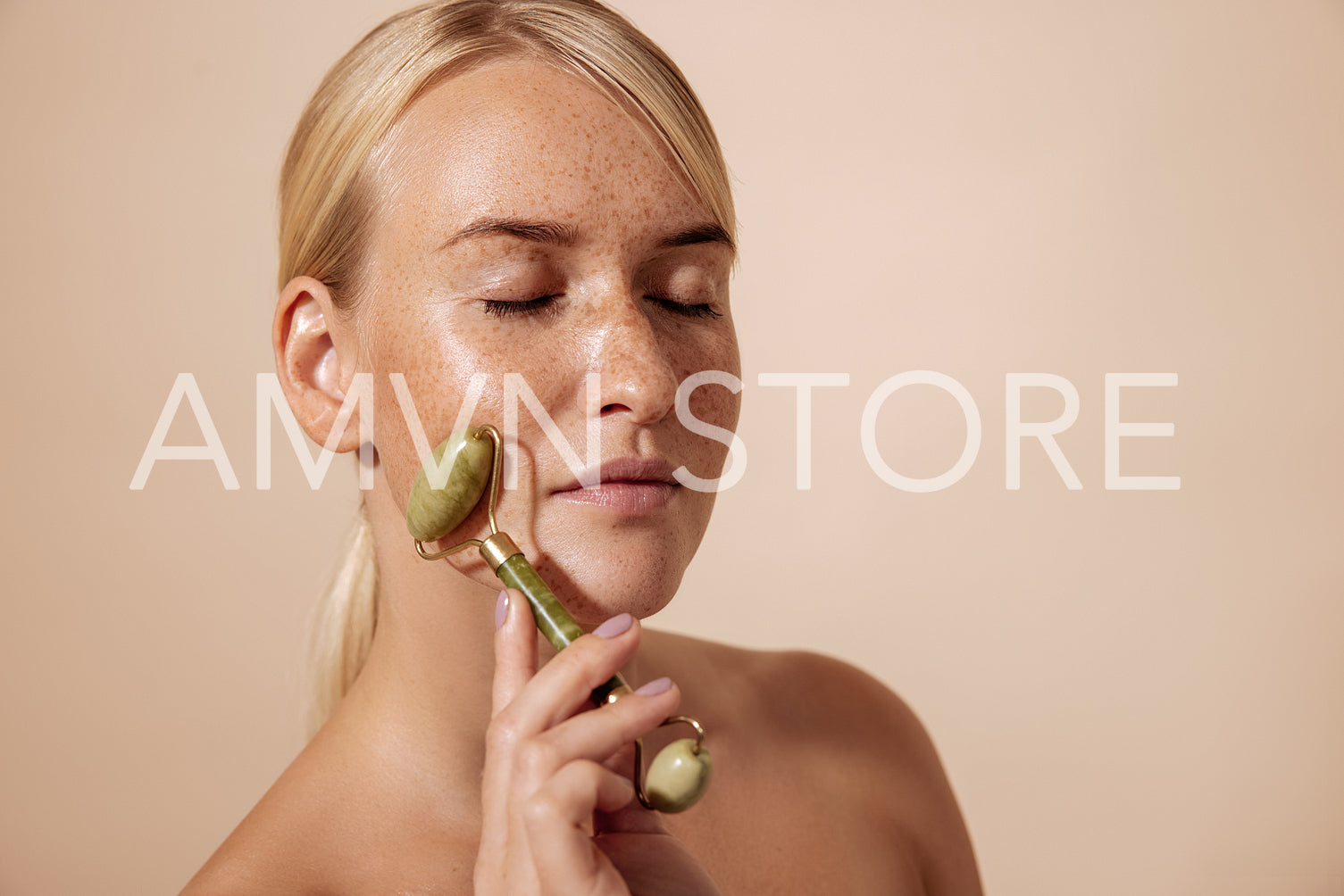 Side view of a young female with freckles massaging face with quartz roller