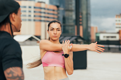 Young female stretching her arm before training on rooftop