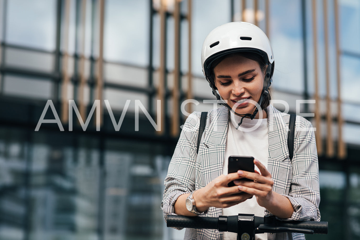 Woman in formal wear typing on smartphone while leaning on the handlebar of electric scooter while standing at an office building