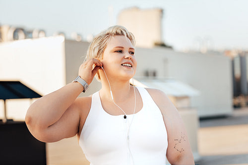 Happy curvy woman standing on a roof. Young oversized female taking a break during exercises.