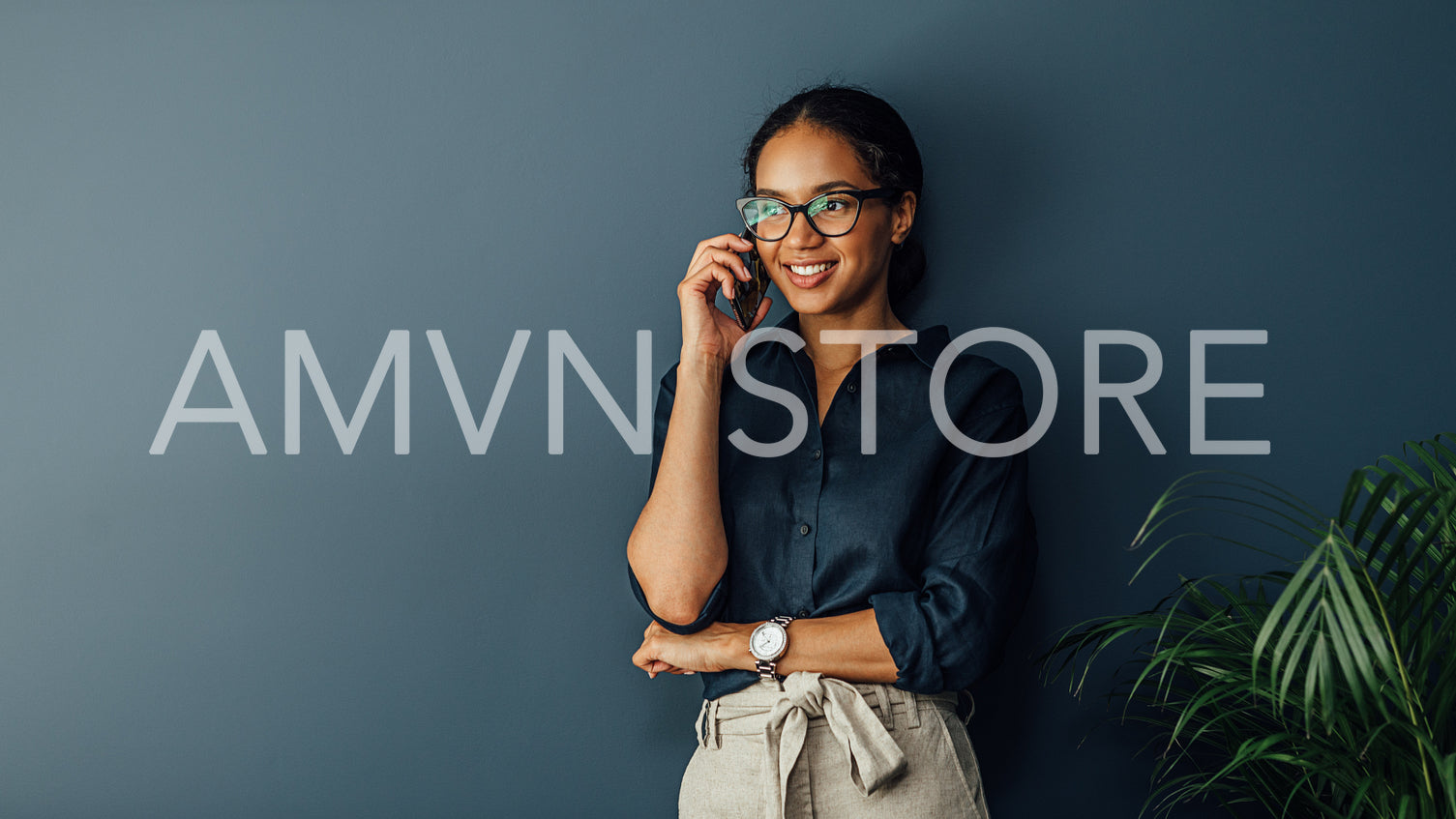 Smiling entrepreneur leaning to a wall in living room while talking on cell phone	