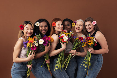 Six smiling women of different ages looking at camera in a studio. Happy diverse females with bouquets and flowers in their hairs standing together.