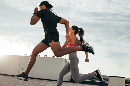 Fitness couple running and jumping on the roof. Athletes sprinting on the roof at sunset.