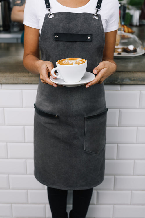 Unrecognizable woman wearing apron, standing in cafe with cup of coffee