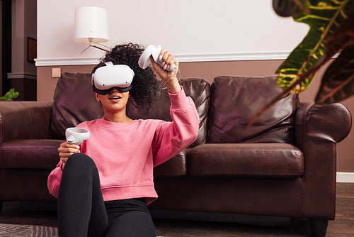 Woman with curly hair wearing VR helmet while sitting in living room at sofa