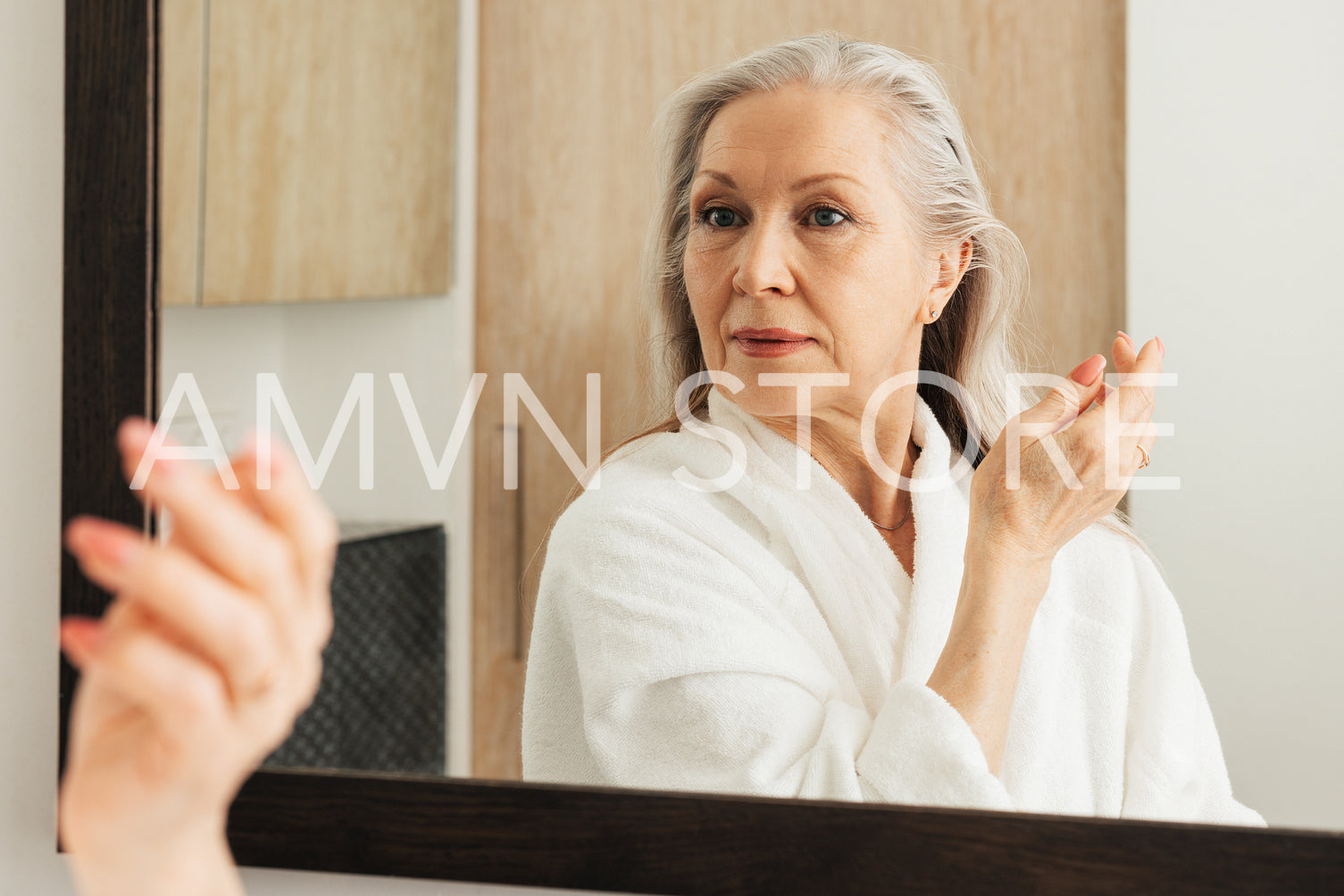 Portrait of an aged woman with grey hair looking at the mirror while standing in a bathroom