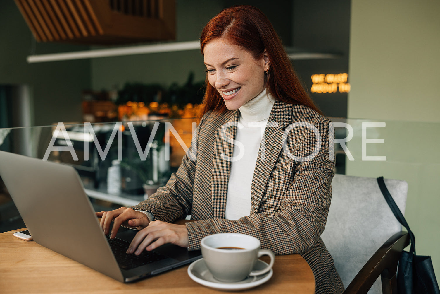 Cheerful woman with ginger hair working in a cafe. Smiling female in formal wear sitting at a table in a coffee shop.