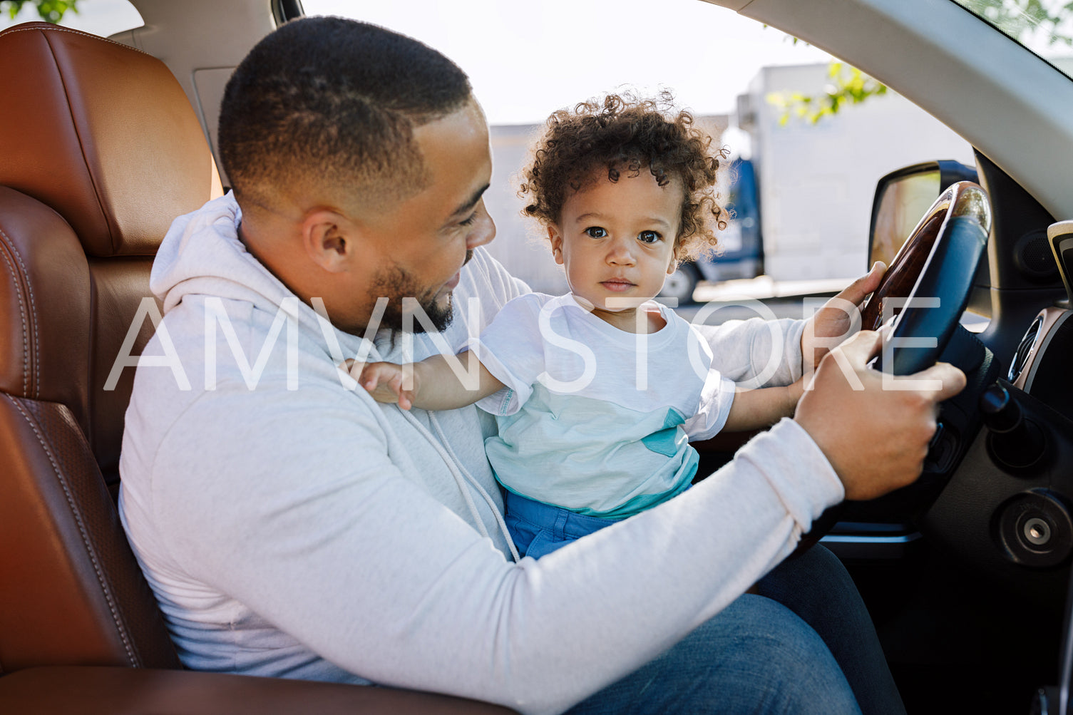 Shot of an adorable little boy sitting on his father's lap in a car and looking at the camera	