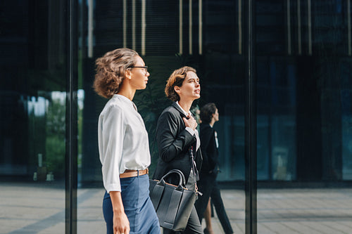 Two businesswomen walking to the office carrying her bags and talking