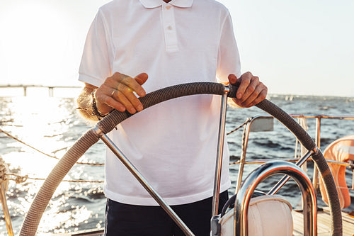 Unrecognizable man standing on a yacht and holding a steering wheel