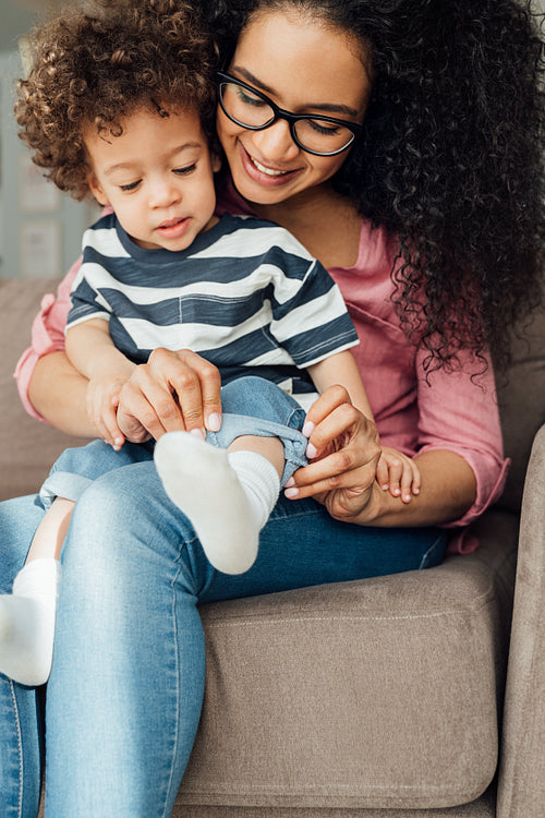 Young mother in eyeglasses helping her son to adjust jeans