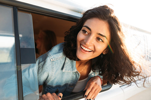 Young happy woman looks out of a camper van window enjoying a road trip