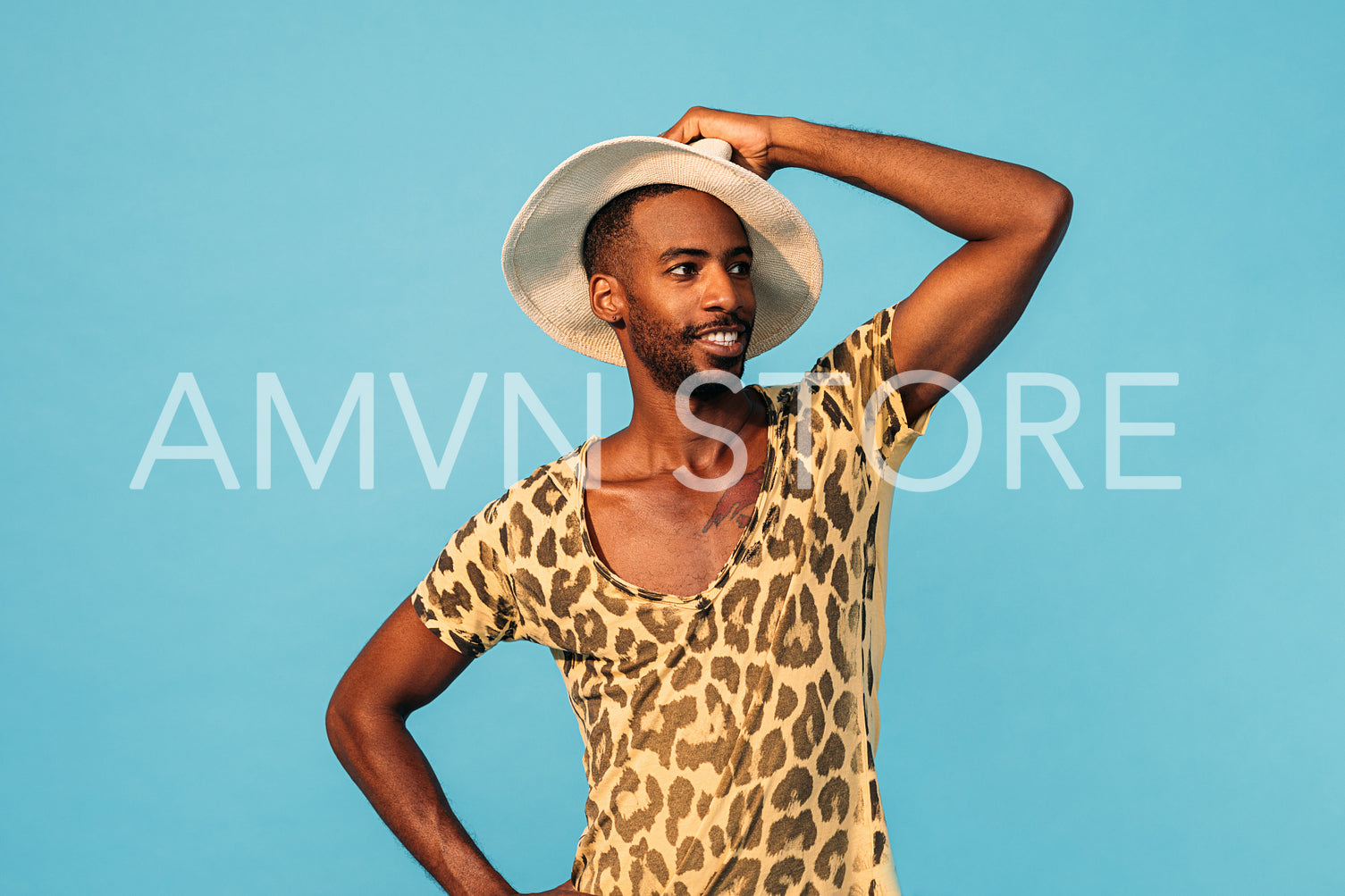 Smiling guy wearing a stylish t-shirt and straw hat looking away while standing against blue background 