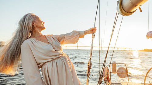 Elderly woman with long hair holding a rope and enjoying sunset on sailboat