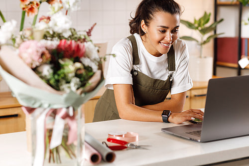 Smiling woman checking new orders on a laptop in her small flower shop