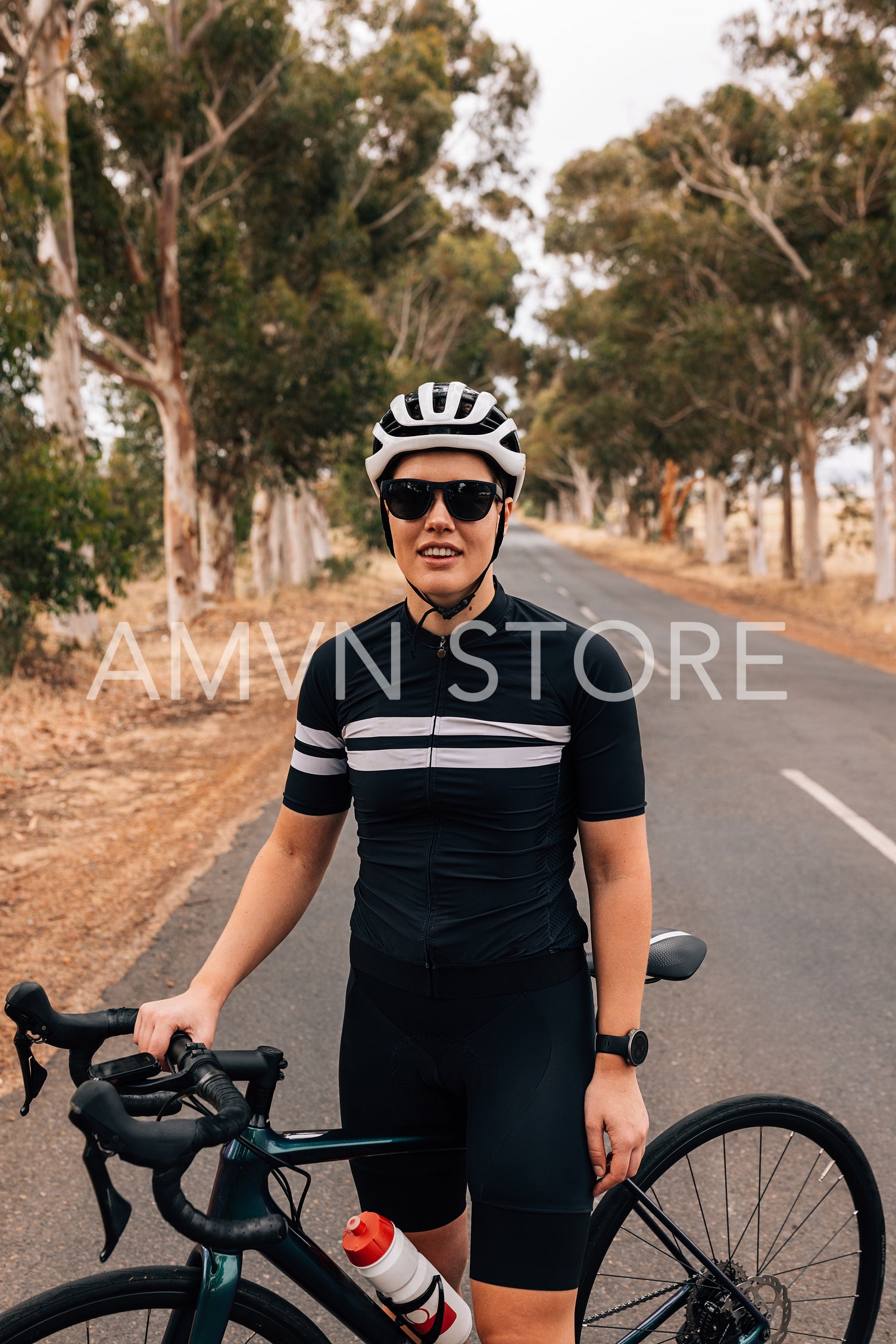 Woman cyclist wearing a helmet and sunglasses standing with his bicycle outdoors on a coutry road