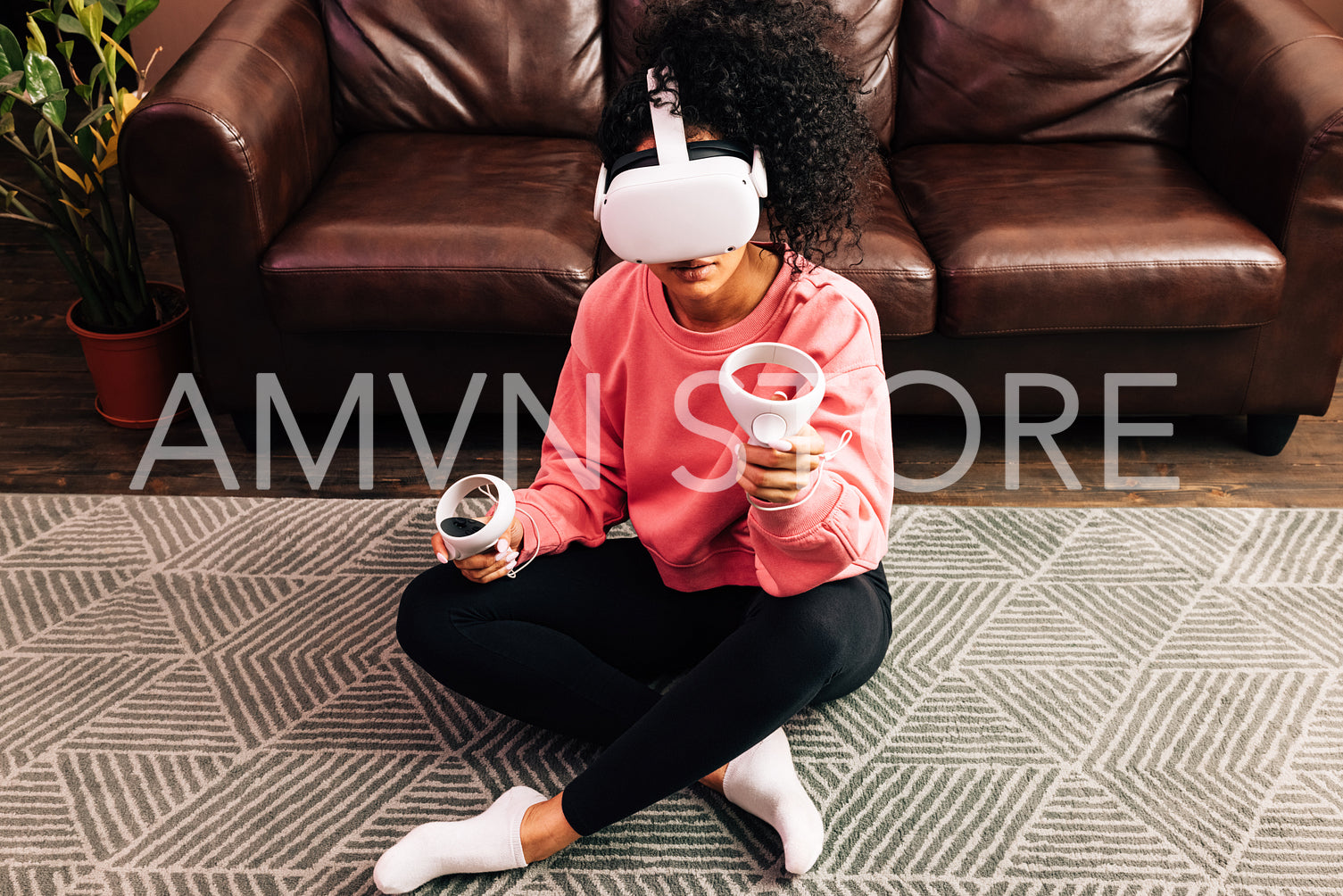 Smiling woman in living room using VR set. Young female in comfy clothes playing video games while sitting on the floor.	