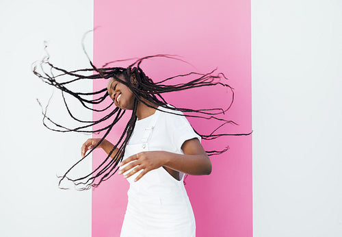 Smiling woman flying her hair in the air at the pink wall outdoors