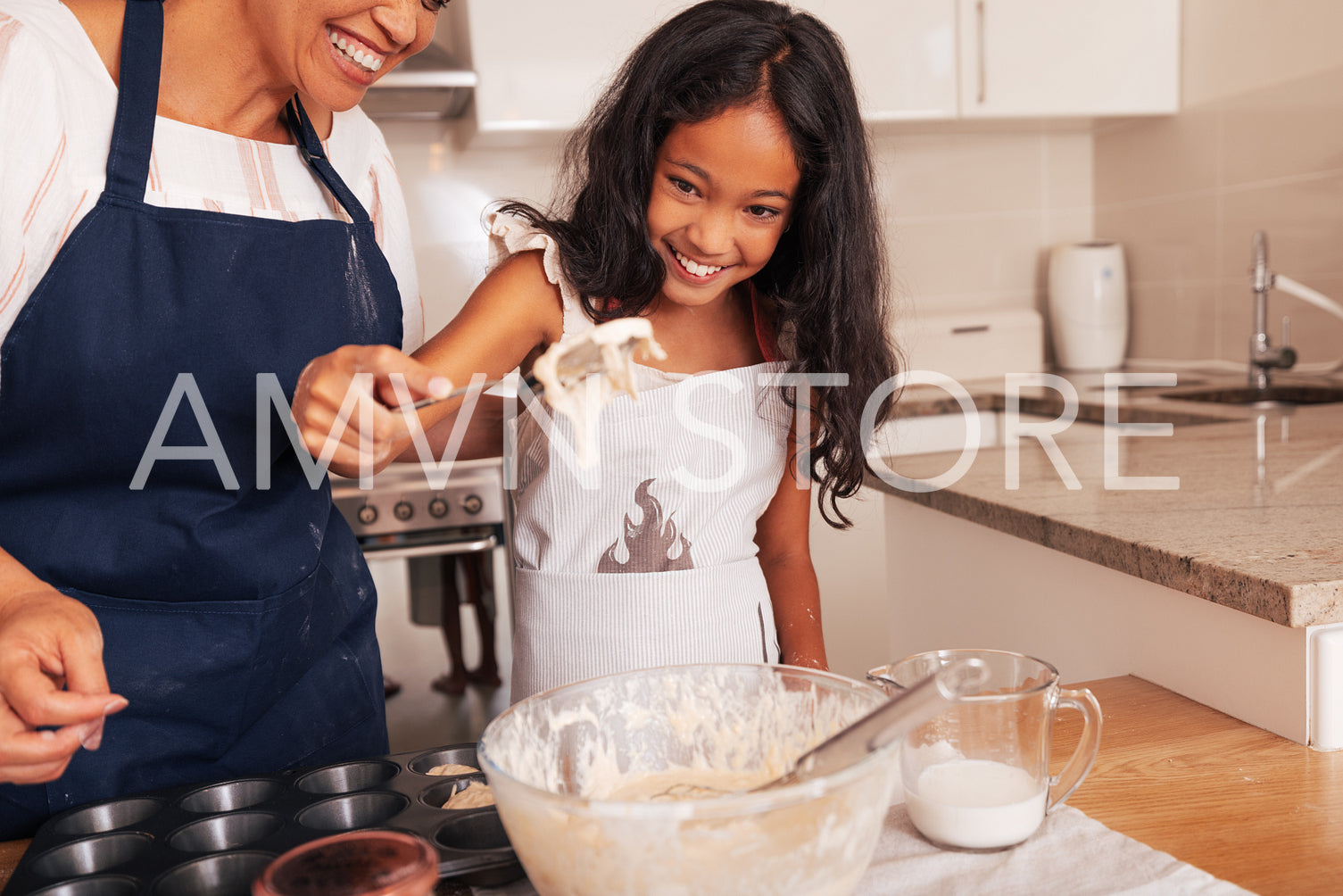 Granny and granddaughter cook together. Happy girl holding a spoon with dough on it.