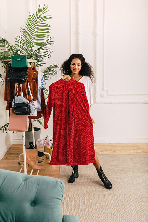 Woman trying on clothes in studio. Fashion stylist standing with red dress.