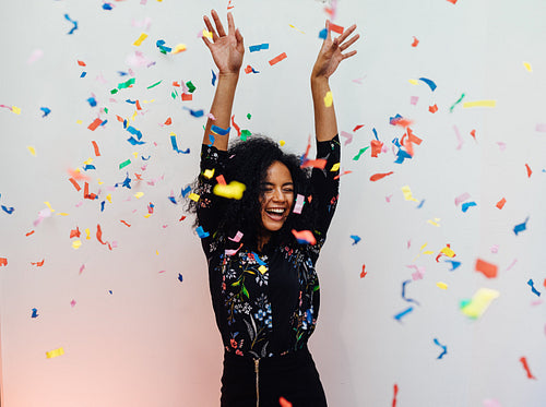 Young beautiful woman laughing under colorful confetti, raised her hands up