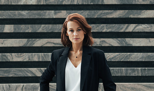 Portrait of a middle-aged female in black formal wear looking at camera. Confident businesswoman posing while standing outdoors.