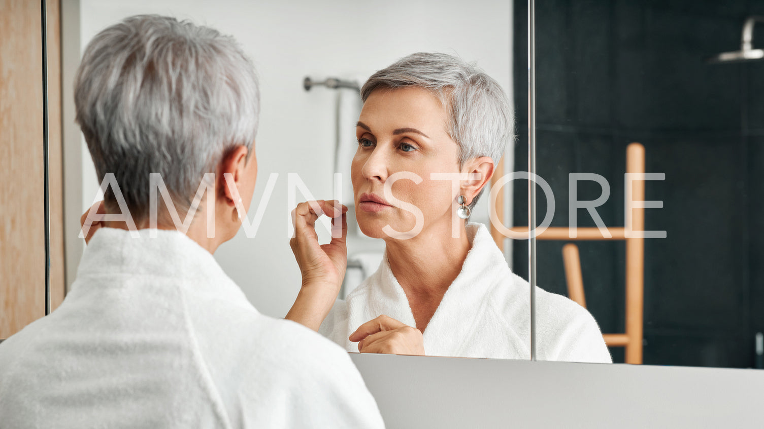 Beautiful senior woman wearing bathrobe standing in front of a mirror	