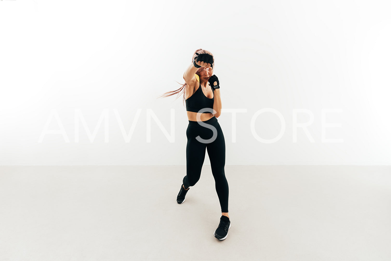 Young woman doing shadow boxing indoors. Muscular female in gloves exercising against a white wall.