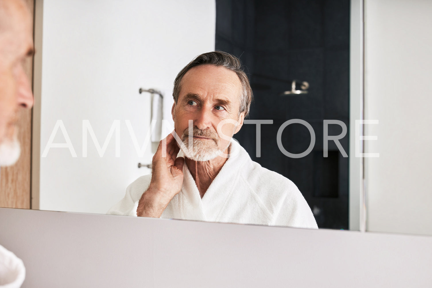 Bearded mature man inspecting his skin in front of a mirror	